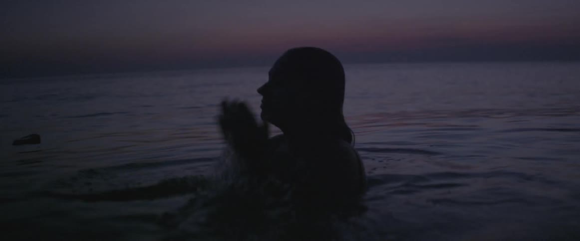 A woman surfaces in the water at sunset