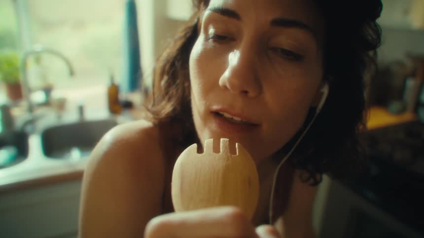 Woman sings up close using a wooden utensil as a microphone