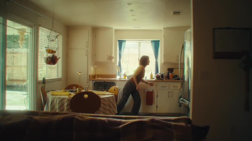 A woman dances through a warmly lit kitchen with sunlight streaming through the window giving the space a cozy livedin feel