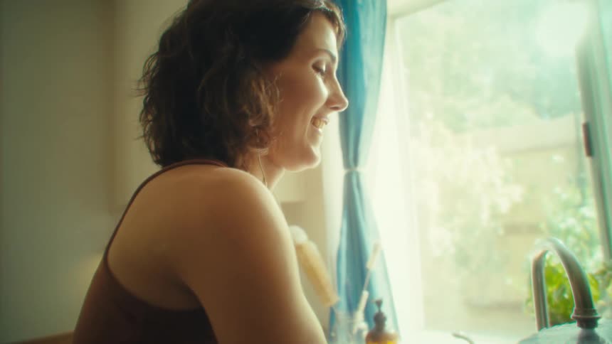 Woman washes pots smiling at the kitchen sink