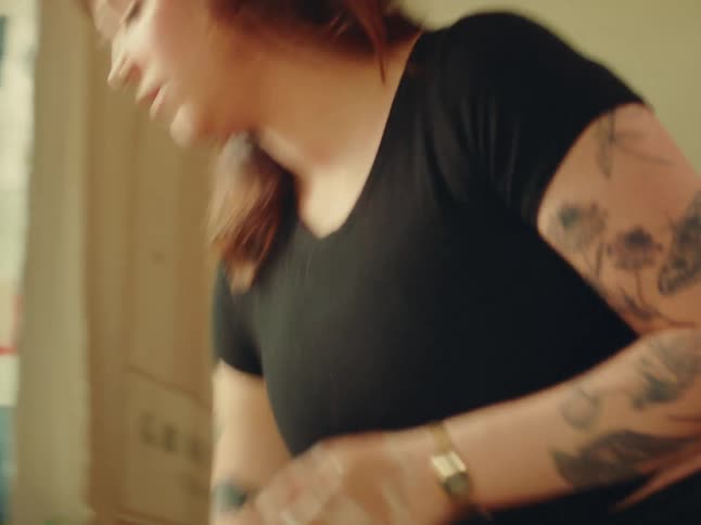Freshly molded ceramic bowls dry on the table as a tattooed person arranges the space
