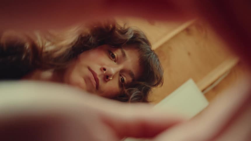 Woman with loose hair and a nose piercing looks downward in a wooden setting