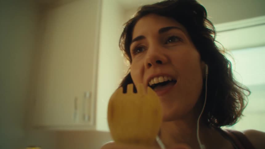 A female cleans a wooden spoon then sings into the spoon in a kitchen