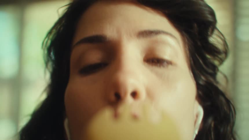 A woman passionately sings into a wooden spoon in a sunlit kitchen