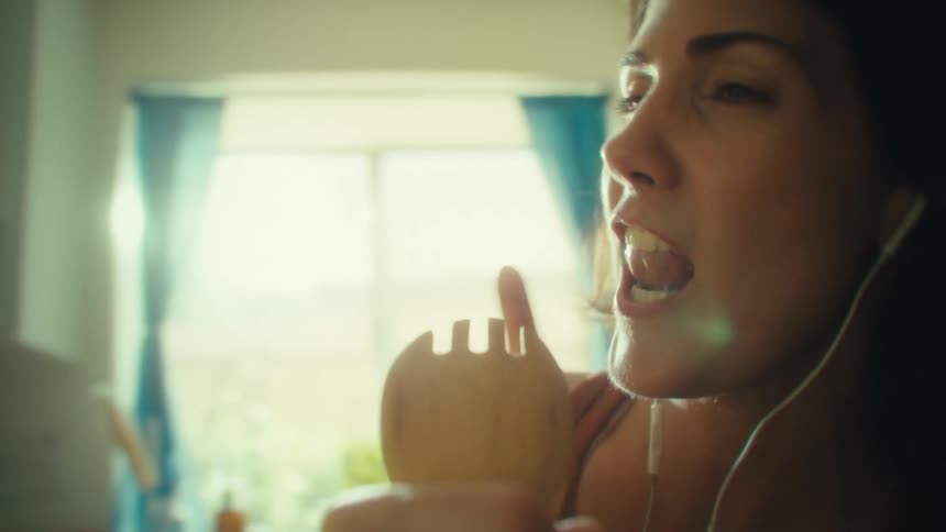 Sunlight bursts through a kitchen window as a woman sings into a wooden spoon in joyful motion