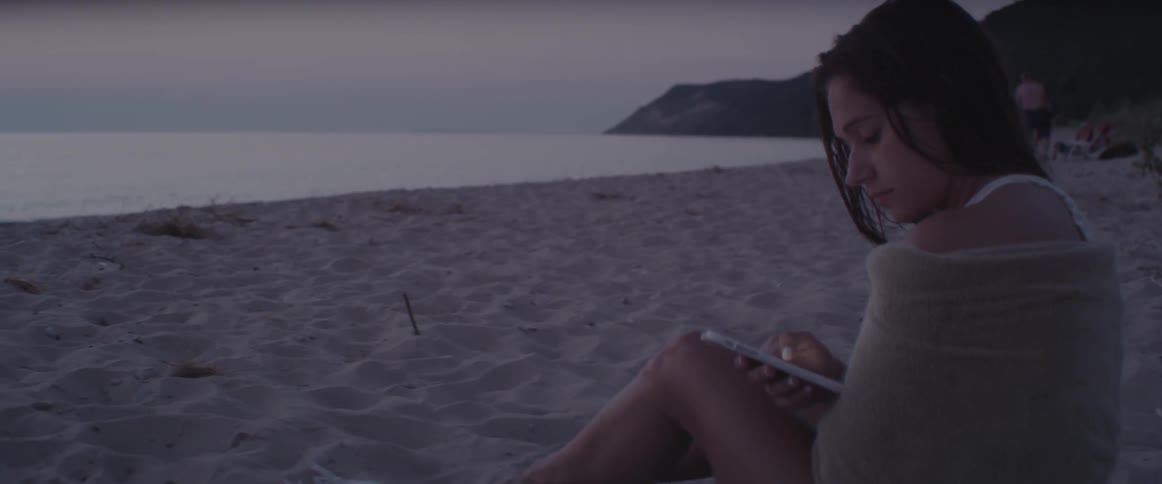 A woman sits on the beach using her phone