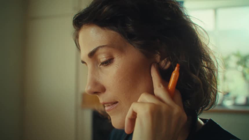 A closeup profile shot of a woman with short dark hair with an orange marker held near her ear
