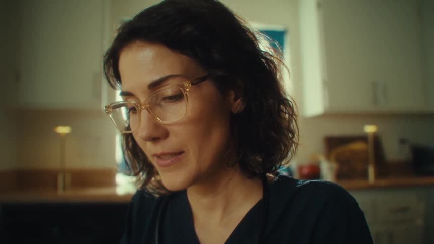 A female in scrubs is sitting at a table reading and talking while holding a chart