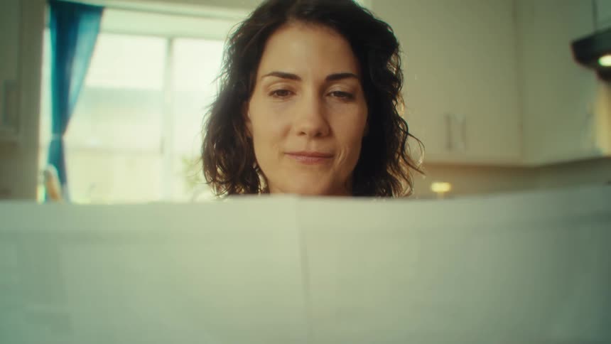 Curlyhaired woman attentively reads a newspaper in a bright setting