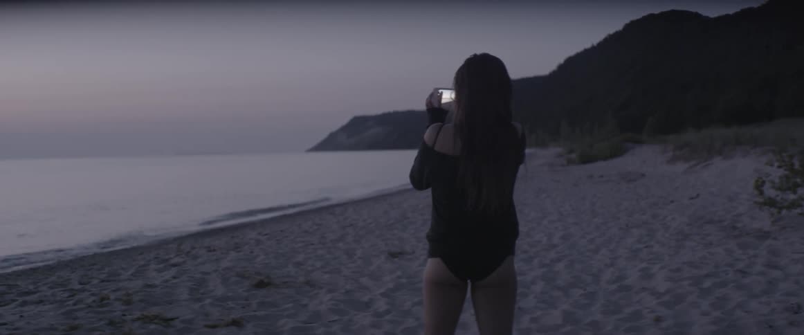 A woman in a swimsuit takes a picture of the ocean at sunset