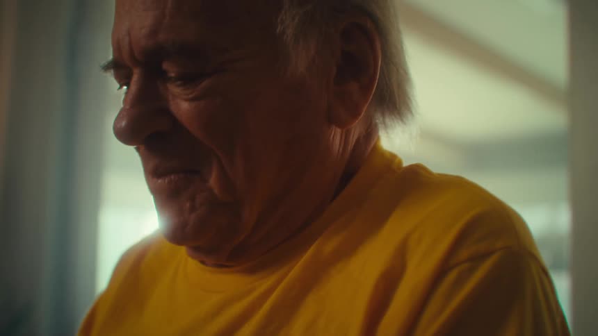 An elderly man smiles gently with emotion his eyes cast downward while he writes in book