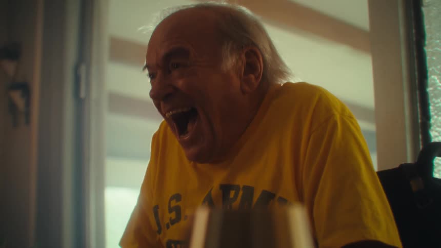 Elderly man in a wheelchair smiles broadly while leaning forward