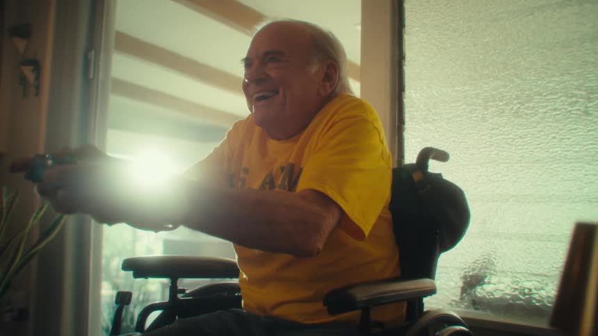 Elderly man in a wheelchair vibrating happily while playing a video game