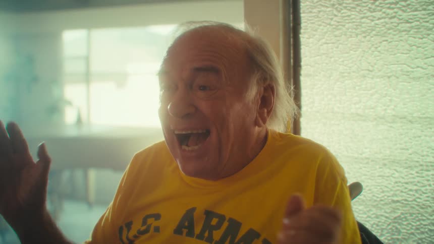 Elderly man in a wheelchair laughs while clapping his hands
