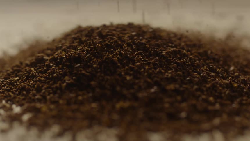 Close up of a mound of ground coffee with more pouring on
