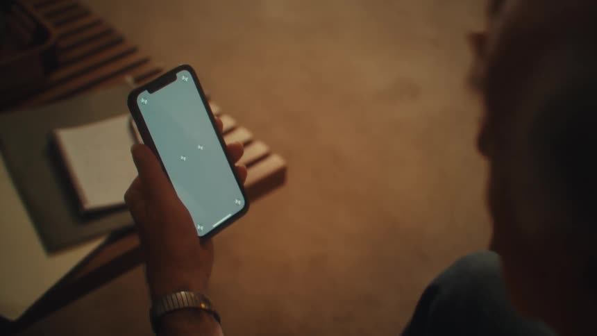 Man holds a lit phone while a notebook rests on the table beside him