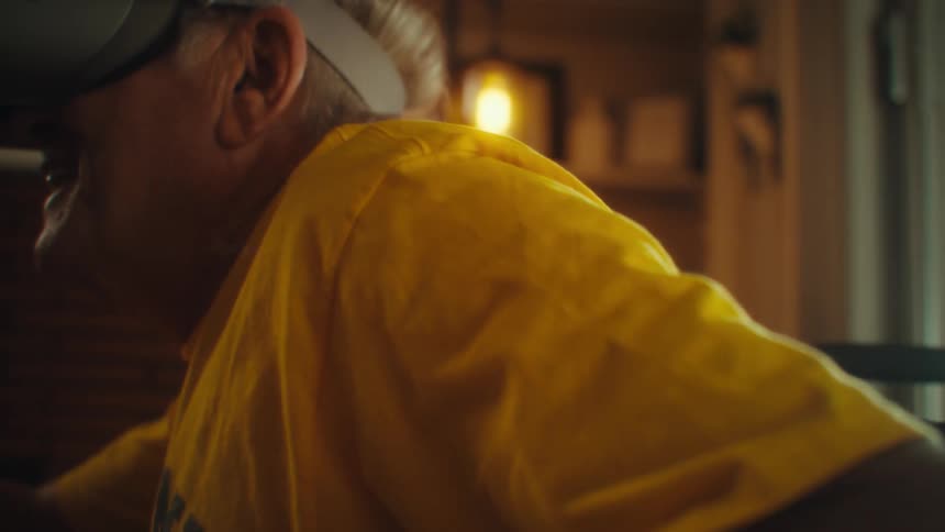 Man in a yellow shirt uses virtual reality goggles while holding a controller