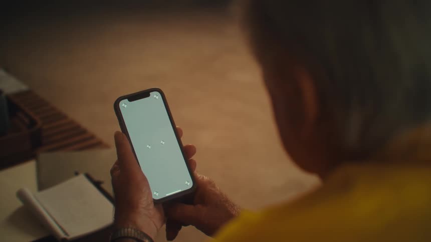 Man holds a lit phone while a notebook rests on the table beside him
