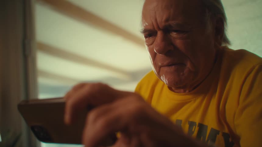 Man in a yellow shirt reacts with surprise while holding a phone