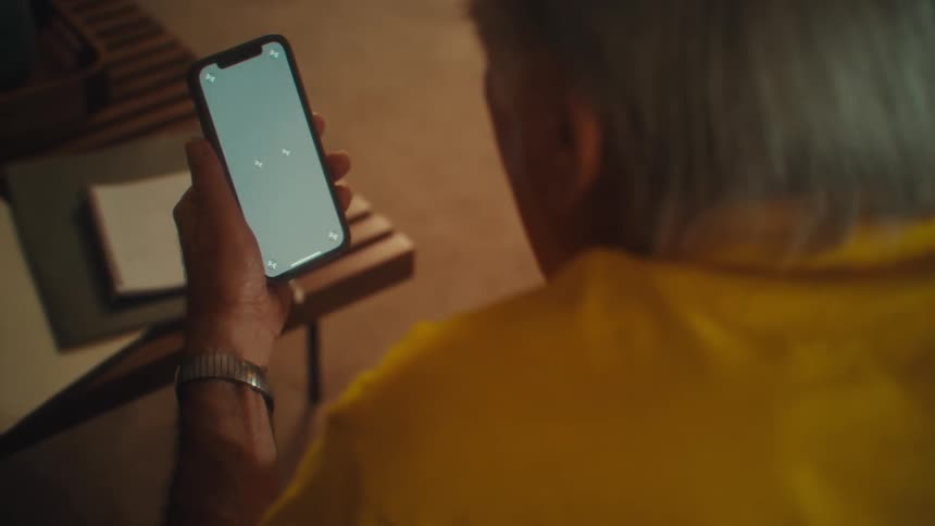 The man is leaning forward looking at his phone screen