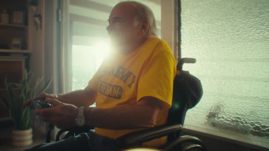 Elderly man in a wheelchair smiles while playing with a video game controller