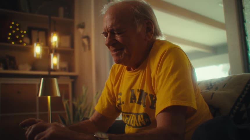 Man in a yellow shirt smiles while holding a phone