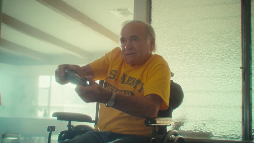 Elderly man in a wheelchair playing a video game with a controller in his hands