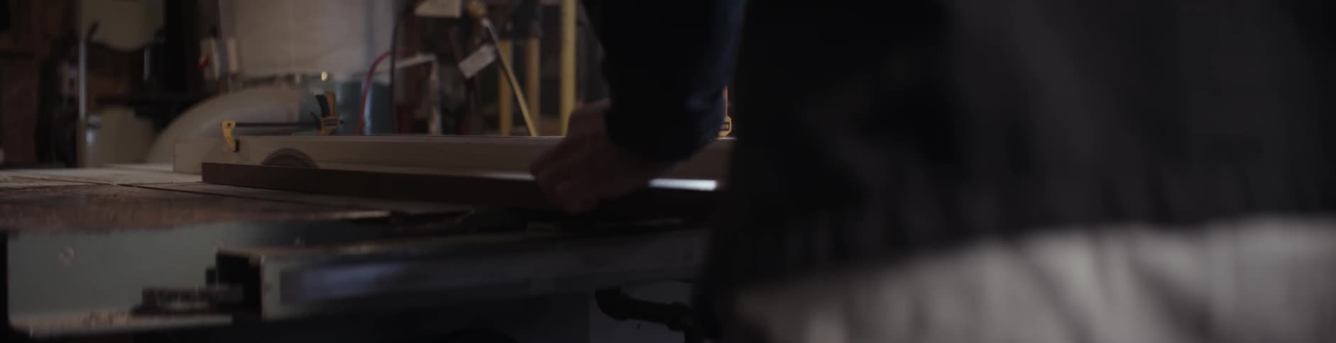 A man is sliding a board on a saw bench