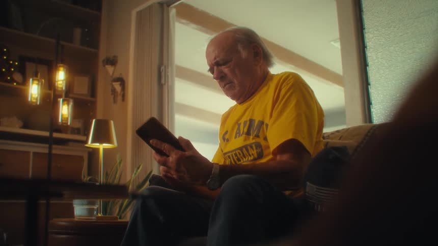 Elderly man picks up a phone call while seated indoors