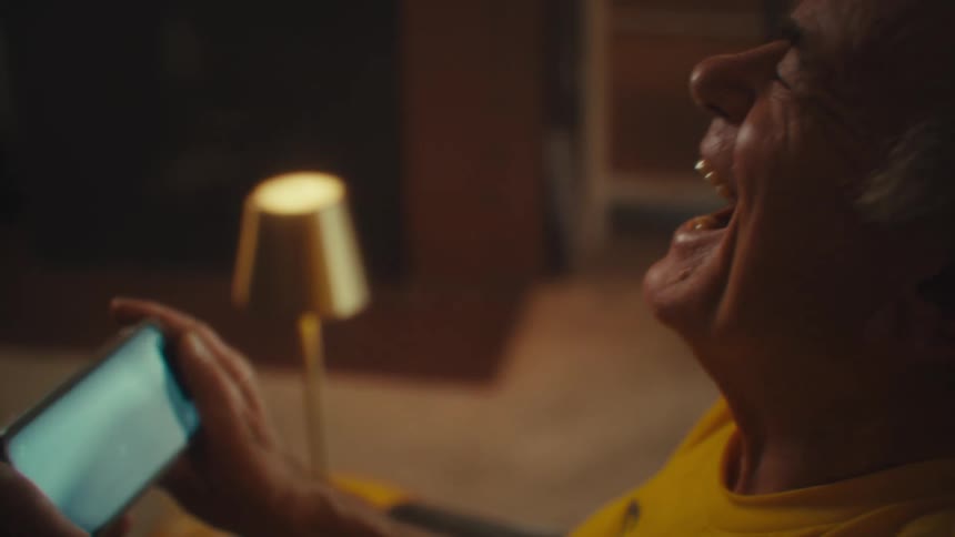 An elderly man smiles while watching his phone