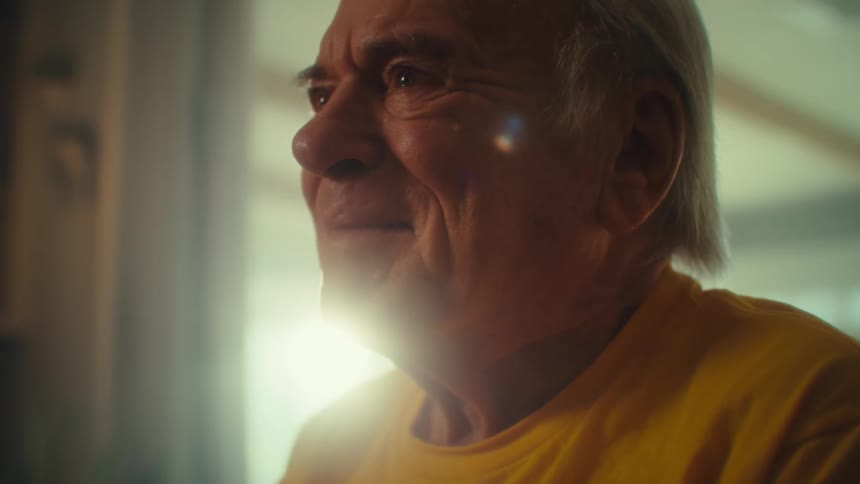 Elderly man in a yellow shirt looks to the side with a calm expression
