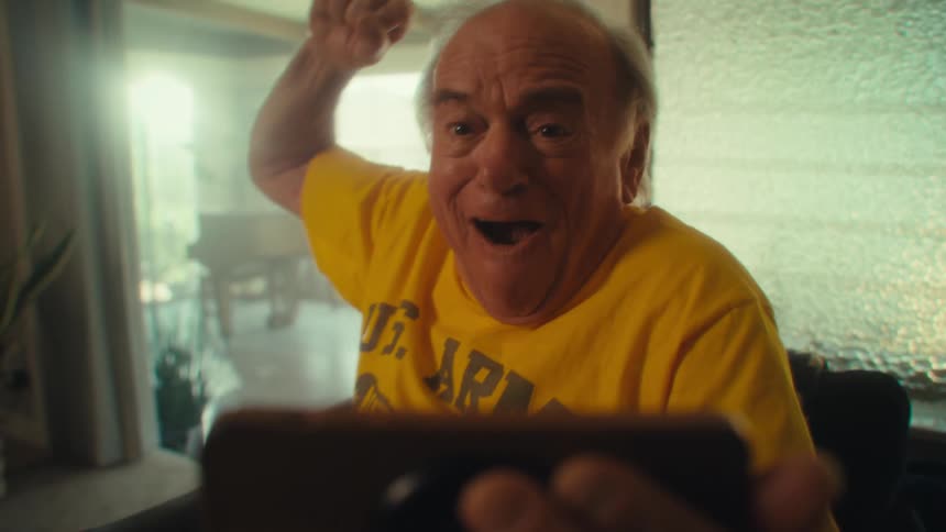 Smiling man in a yellow shirt celebrates while holding a phone