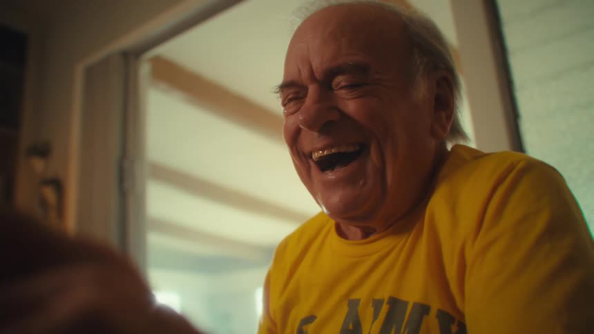 Man in a yellow shirt smiles broadly in a welllit setting