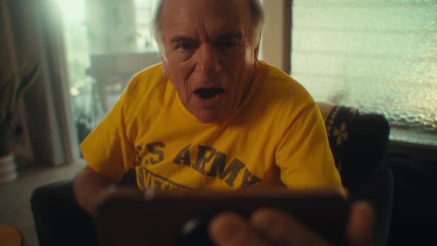Man in a yellow shirt cheers excitedly while looking at a phone
