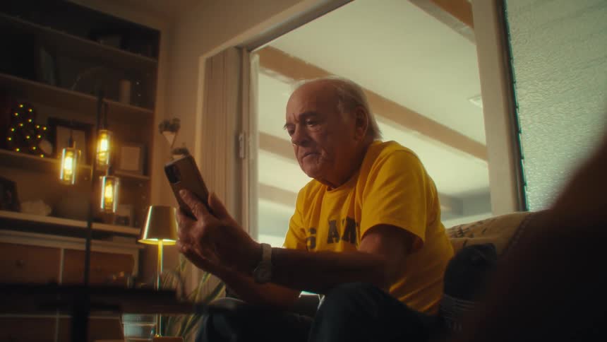 Elderly man in yellow tshirt makes surprised expression after picking up a cell phone