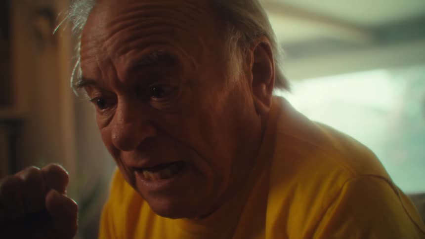 Man in a yellow shirt closely watches the screen of a phone he holds with both hands