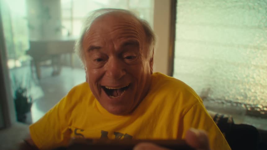Man in a yellow shirt raises his arm in celebration while holding a phone