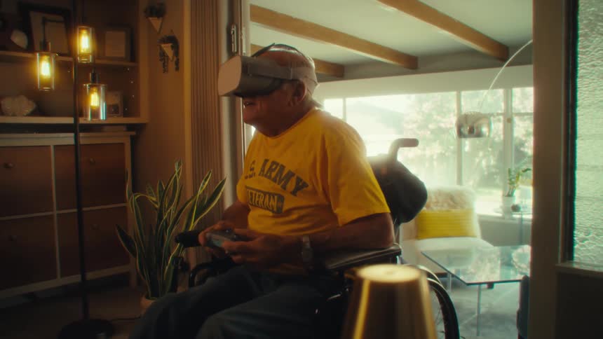 Elderly man in a wheelchair uses virtual reality headset with controller in hand
