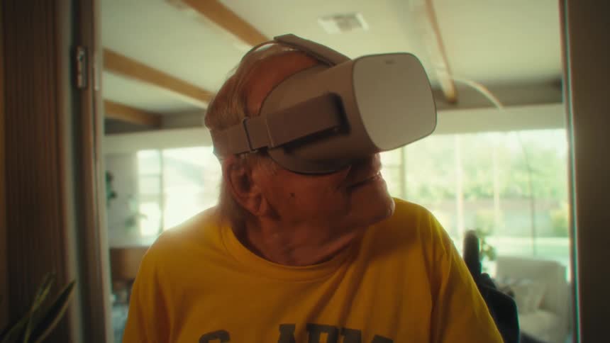 An elderly man wearing a vr headset having fun and excited while sitting in a wheelchair at midday in his living room