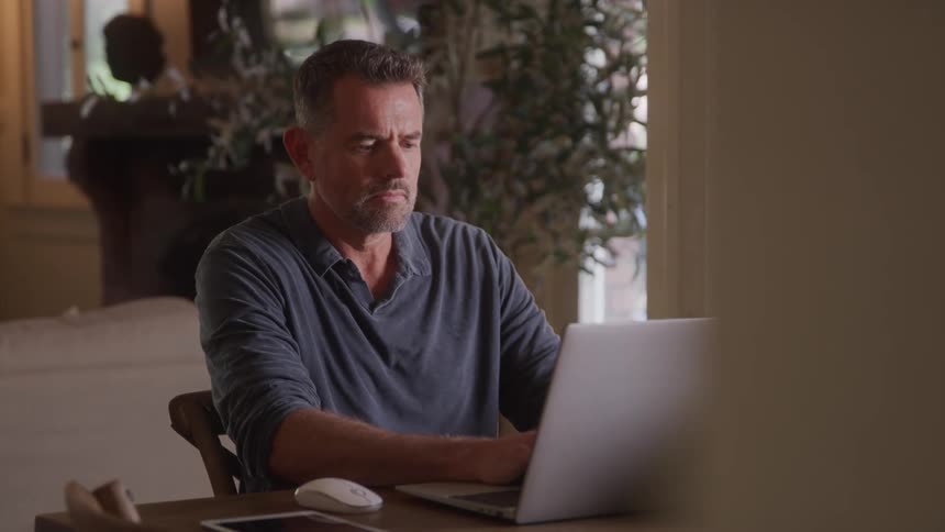 Man with short beard works on a laptop at a wooden table