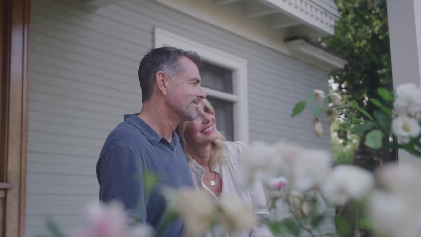 A husband and wife are smiling on the porch