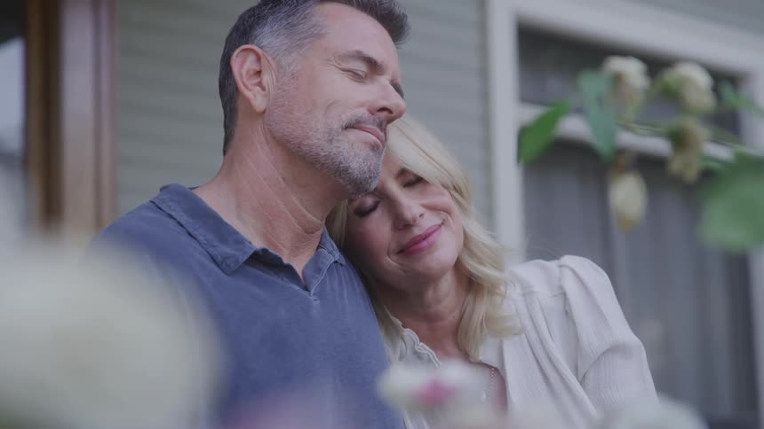 A content middleaged couple embraces tenderly on a porch