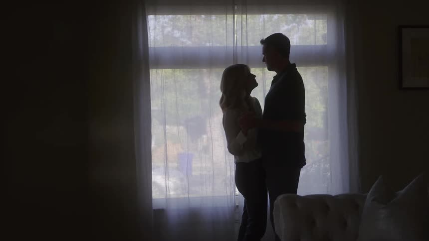 Couple embraces in front of a window lit by soft light