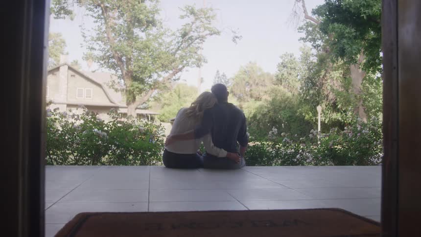 Couple sitting with their backs turned on a porch hugging while looking at the garden
