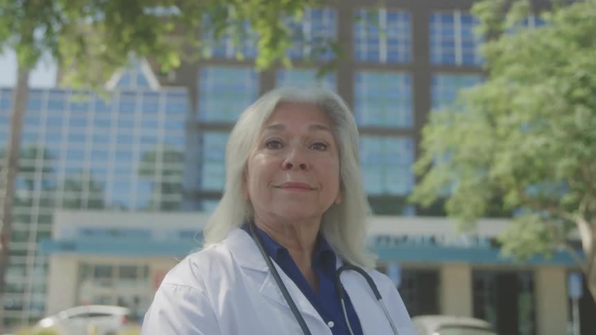 A confident female doctor stands outside a modern hospital building