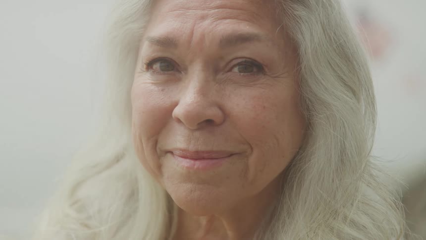 The video shows a closeup of an elderly womans face with long gray hair and a warm smile she looks happy and content