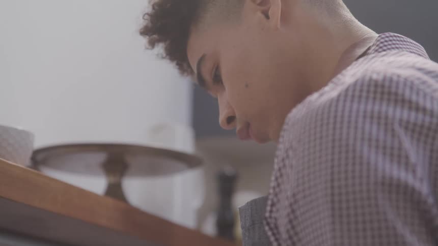 The video shows a closeup of a young persons head and shoulders with curly hair and a beanie the person is looking down seemingly focused on something just out of frame