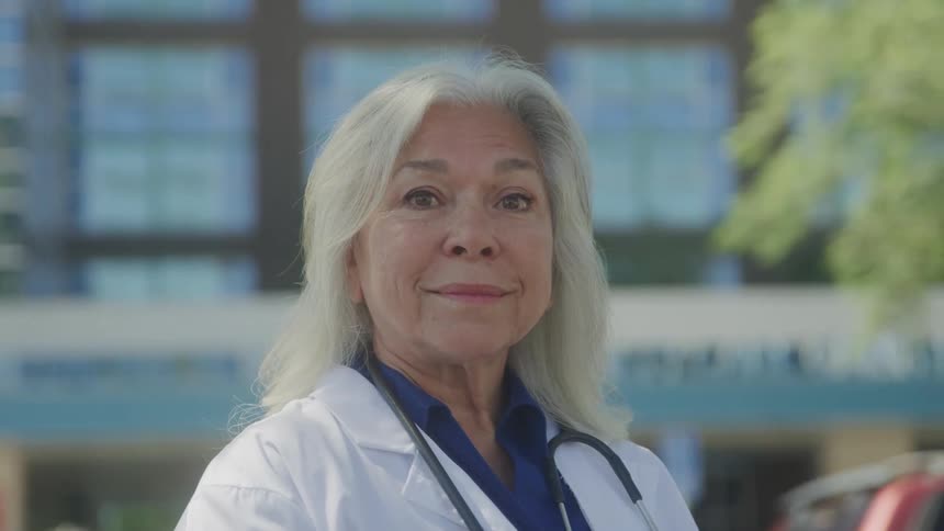 The video shows a closeup of a smiling elderly woman with long gray hair she is wearing a white doctors coat and a stethoscope suggesting she is a physician or a healthcare professional