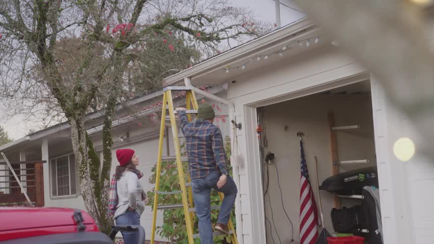 A man hangs christmas lights over the garage