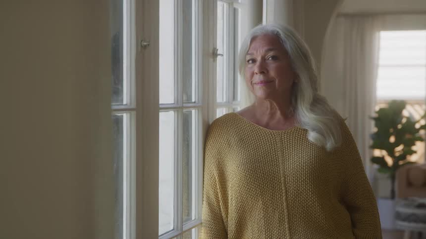 The video shows a closeup of an elderly woman with long gray hair looking out a window she has a calm and peaceful expression on her face